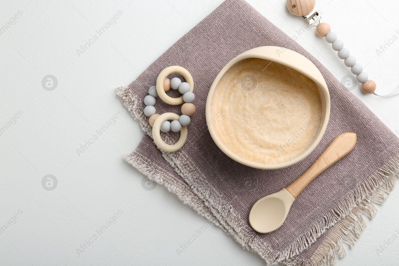 Photo of Delicious baby food in bowl with spoon and teether on white background, flat lay. Space for text