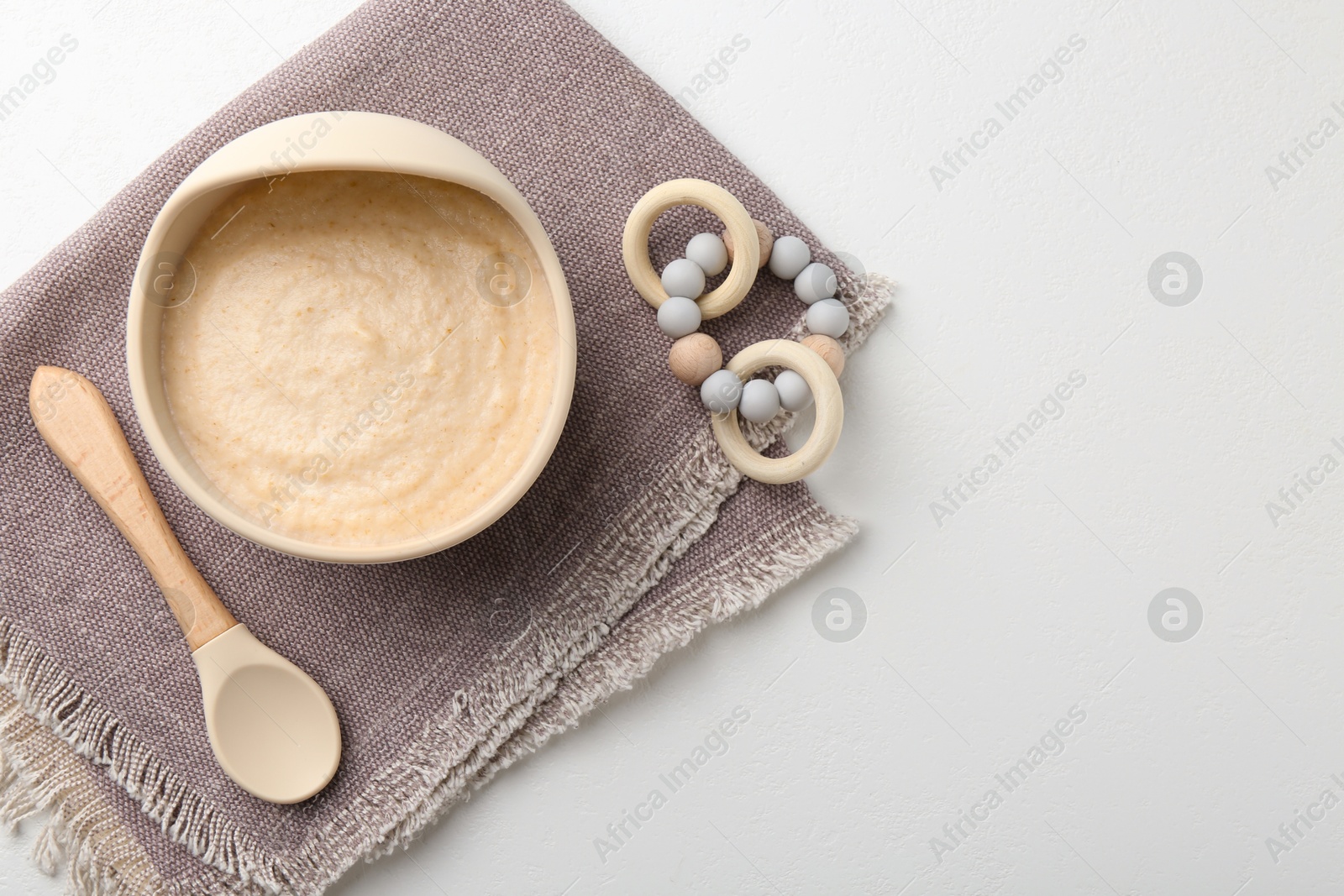 Photo of Delicious baby food in bowl with spoon and teether on white background, flat lay. Space for text