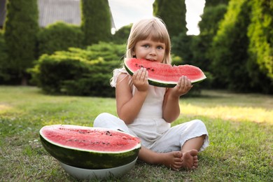 Photo of Cute little girl eating juicy watermelon on green grass outdoors