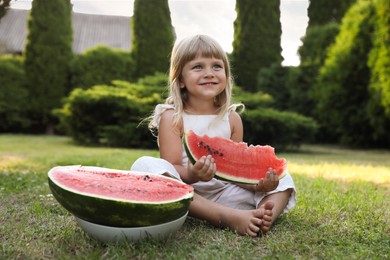 Photo of Cute little girl eating juicy watermelon on green grass outdoors