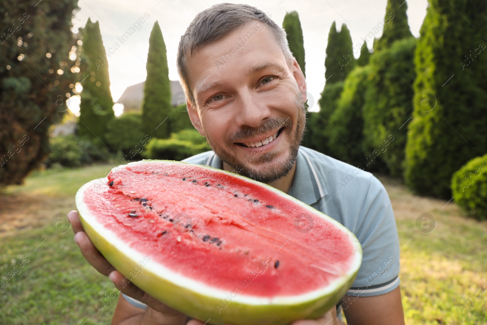 Photo of Happy man with half of juicy watermelon outdoors