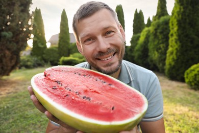 Photo of Happy man with half of juicy watermelon outdoors