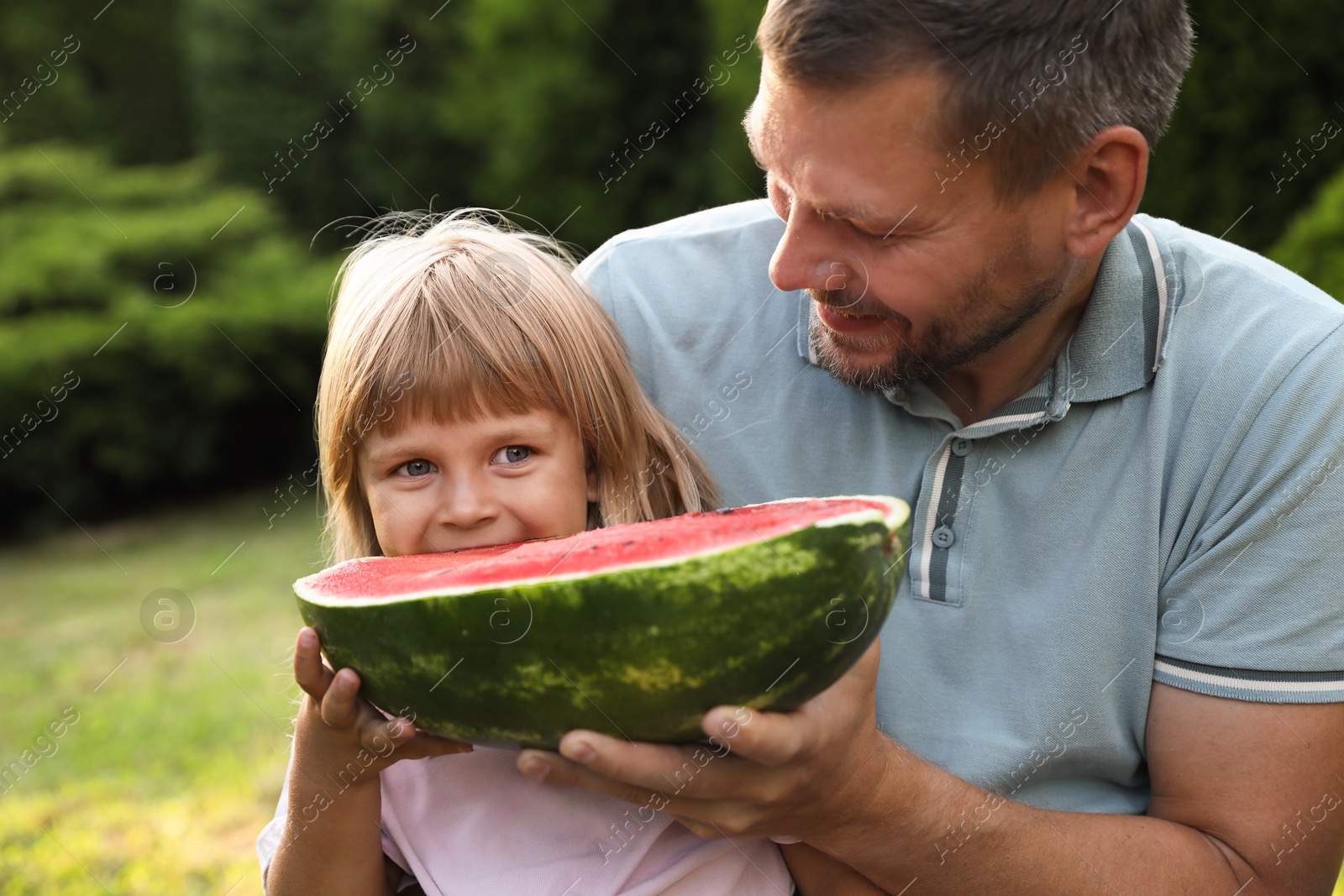 Photo of Man and his cute daughter eating juicy watermelon outdoors together