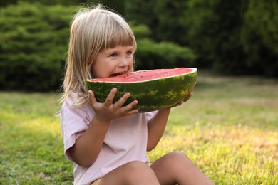 Photo of Cute little girl with half of juicy watermelon on green grass outdoors