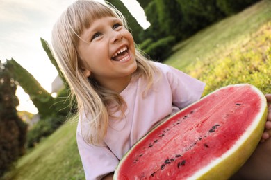 Cute little girl with half of juicy watermelon on green grass outdoors