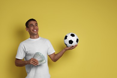 Happy man with money and soccer ball on yellow background, space for text