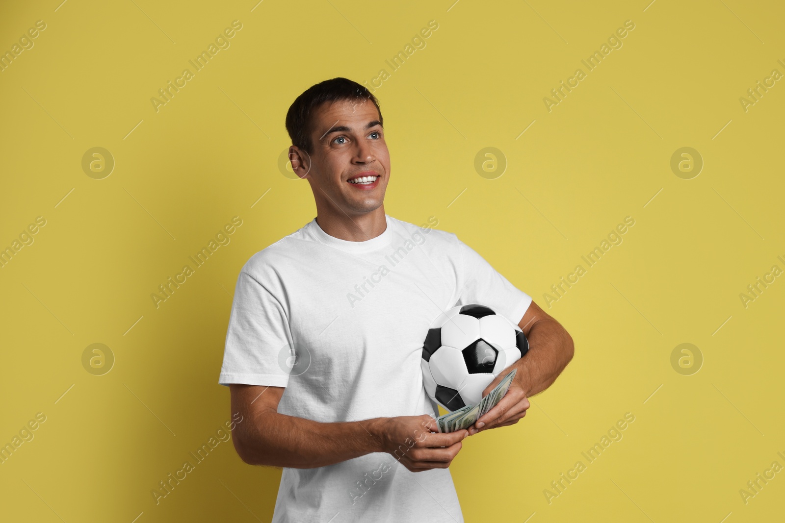 Photo of Happy man with money and soccer ball on yellow background