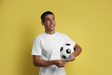 Happy man with money and soccer ball on yellow background