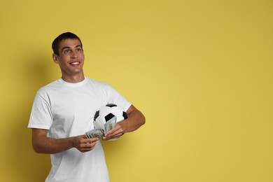 Photo of Happy man with money and soccer ball on yellow background, space for text