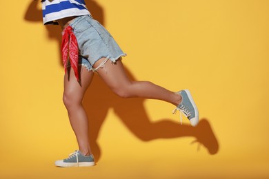 Woman wearing stylish denim shorts on yellow background, closeup