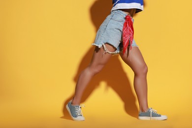 Woman wearing stylish denim shorts on yellow background, closeup