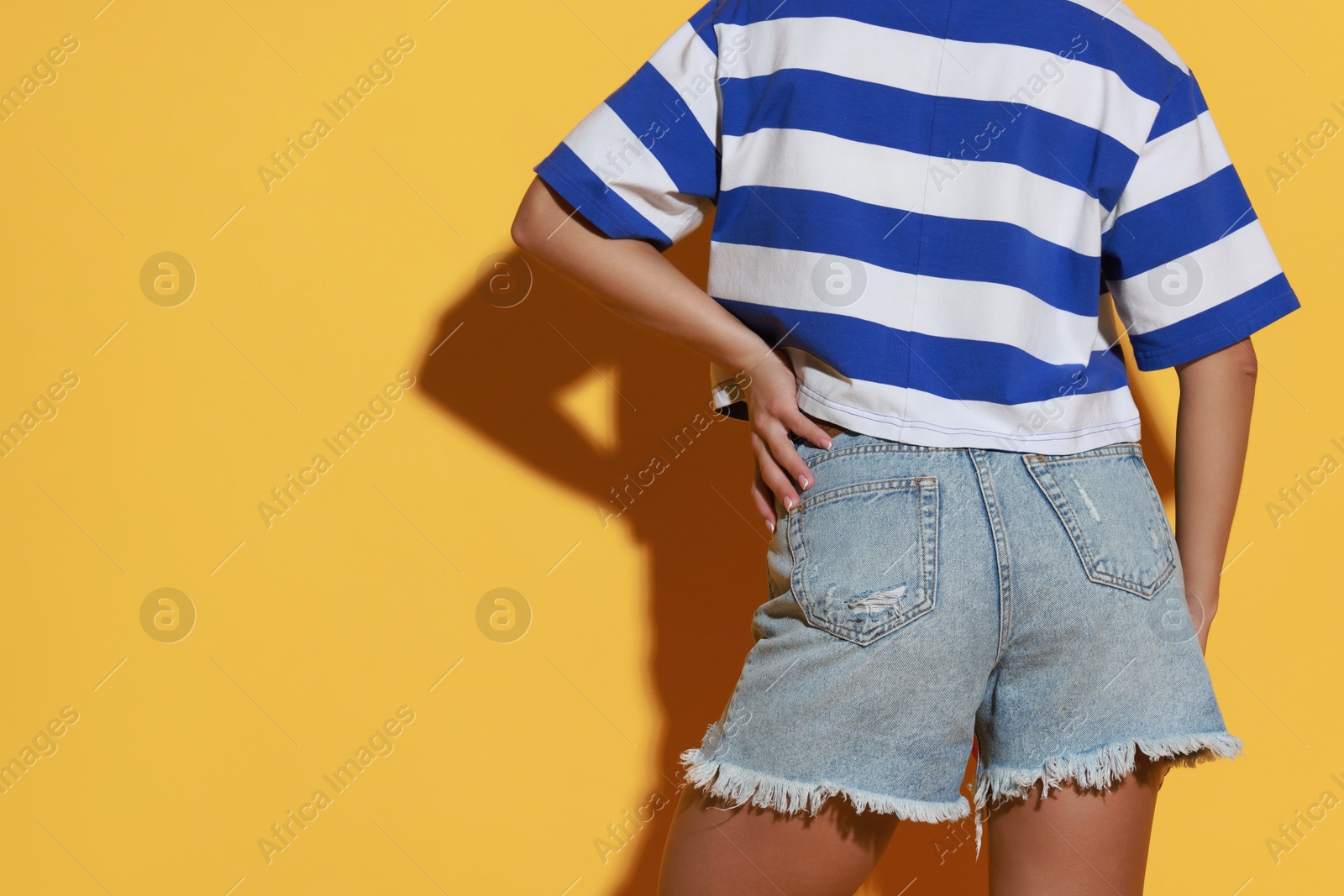 Photo of Woman wearing stylish denim shorts on yellow background, closeup. Space for text