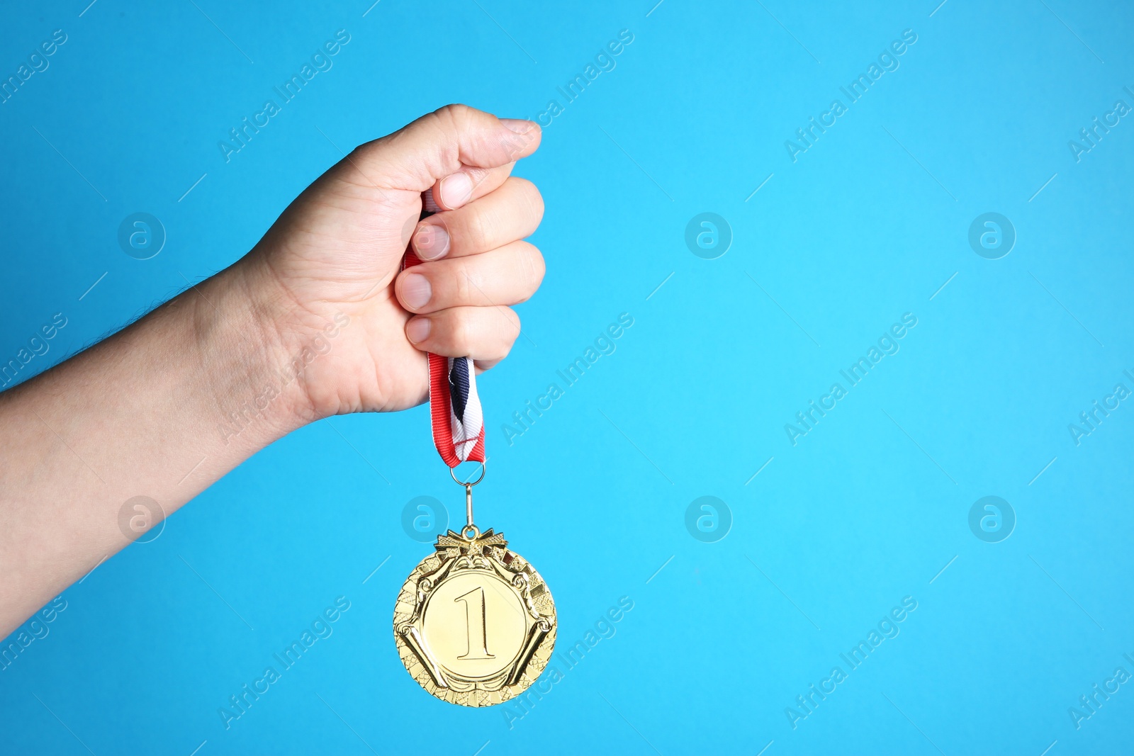 Photo of Man with golden medal on light blue background, closeup. Space for text