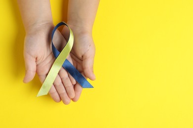 Photo of Child with yellow and blue ribbon on color background, top view. Down syndrome awareness