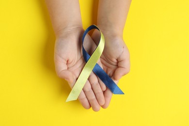 Child with yellow and blue ribbon on color background, top view. Down syndrome awareness