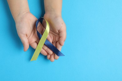 Photo of Child with yellow and blue ribbon on color background, top view. Down syndrome awareness