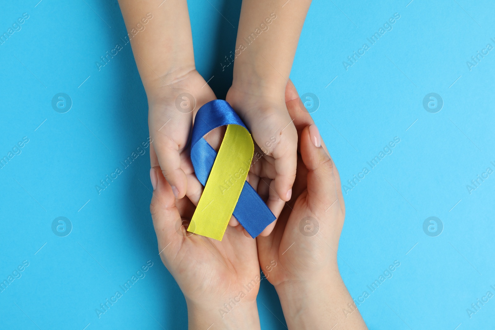 Photo of Woman with child holding yellow and blue ribbons on color background, top view. Down syndrome awareness