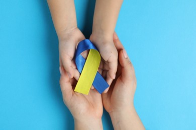 Photo of Woman with child holding yellow and blue ribbons on color background, top view. Down syndrome awareness