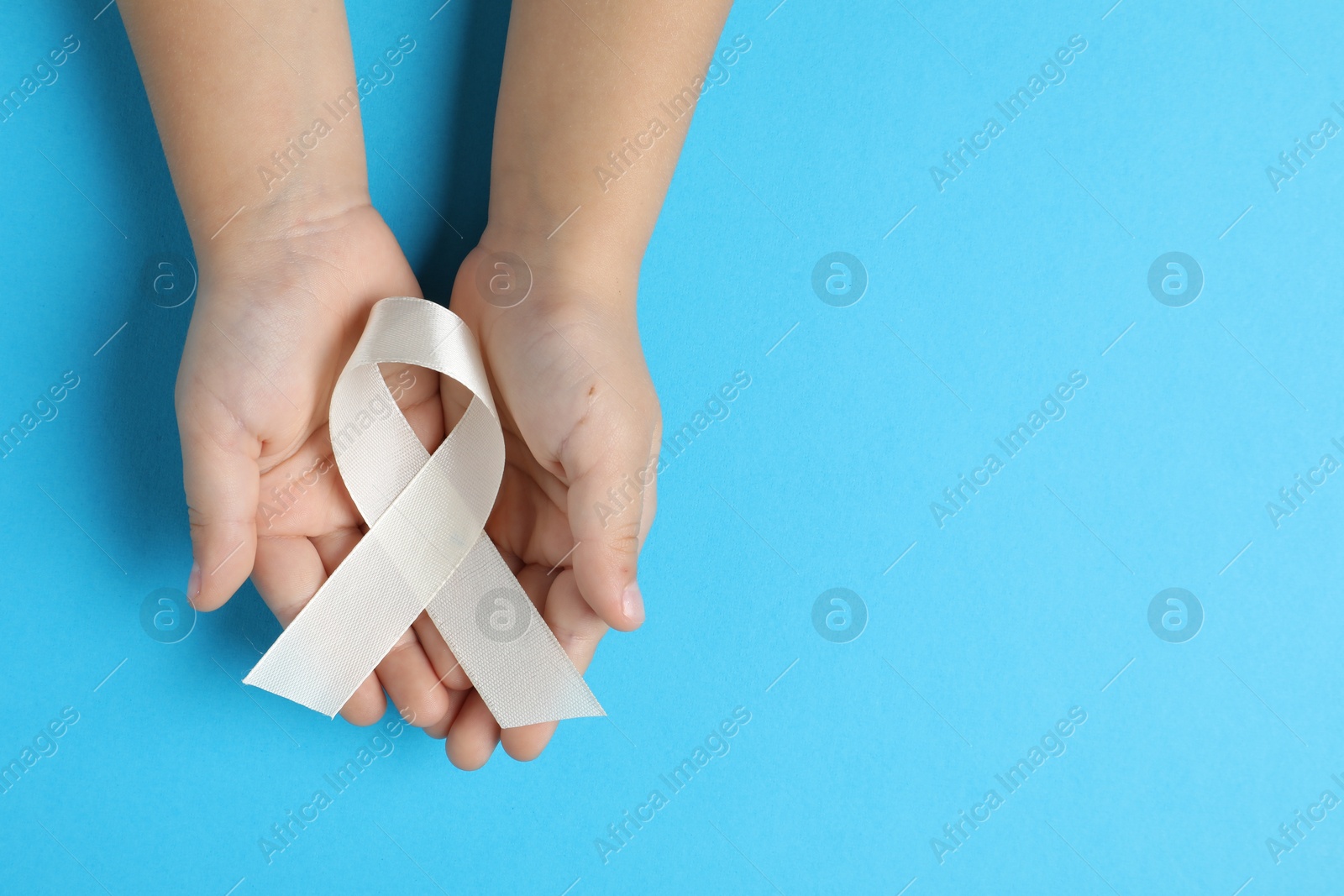 Photo of Child with white ribbon on light blue background, top view and space for text. Bone cancer and lung disease awareness