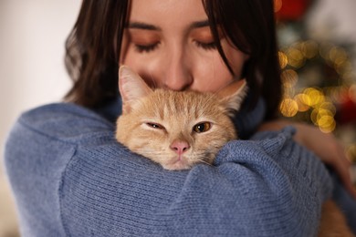 Photo of Woman with cute ginger cat in room decorated for Christmas, closeup