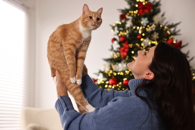 Photo of Woman with cute ginger cat in room decorated for Christmas