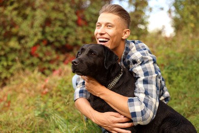 Smiling man hugging cute dog outdoors on autumn day. Space for text