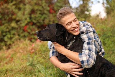 Photo of Smiling man hugging cute dog outdoors on autumn day. Space for text