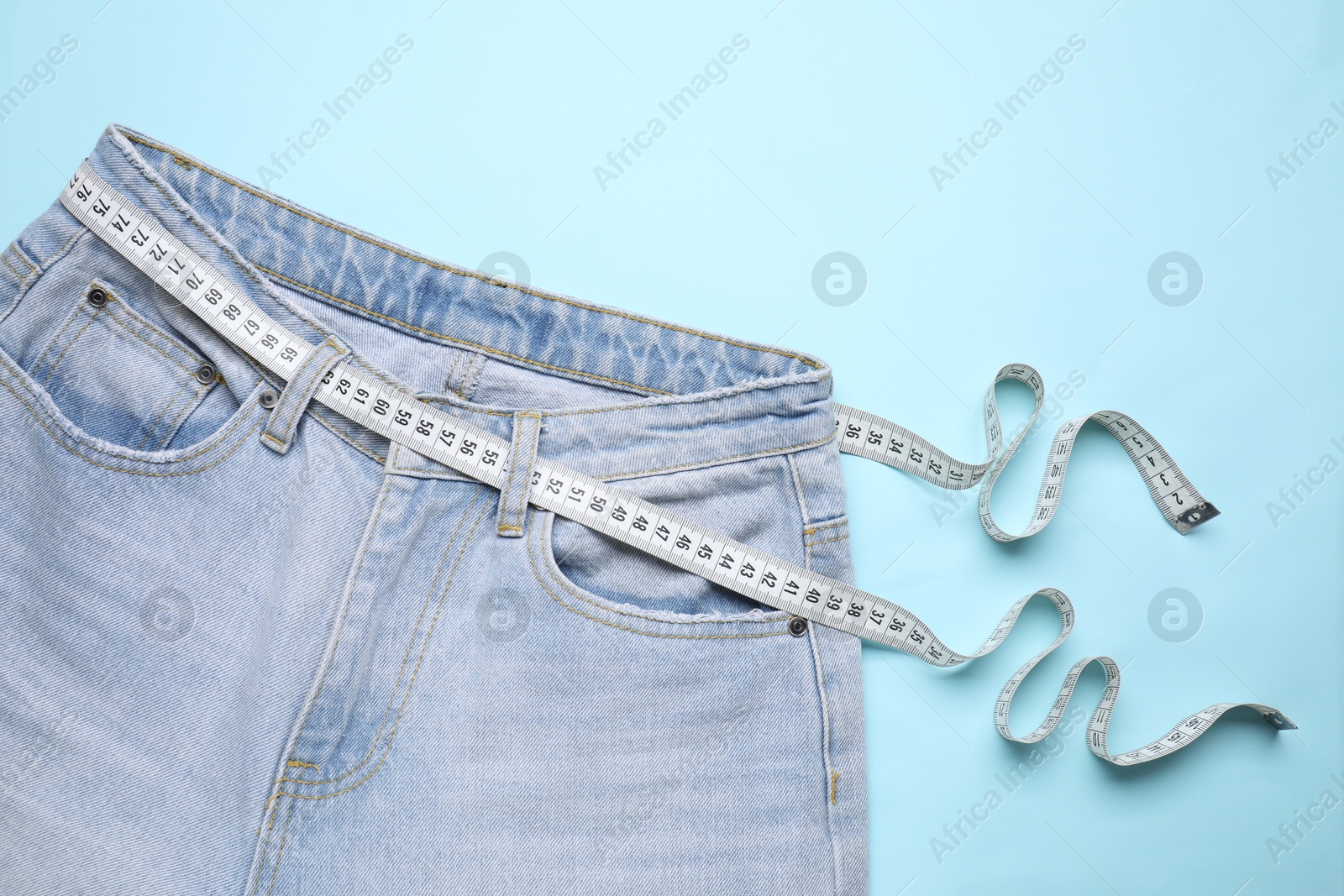 Photo of Jeans and measuring tape on light blue background, top view