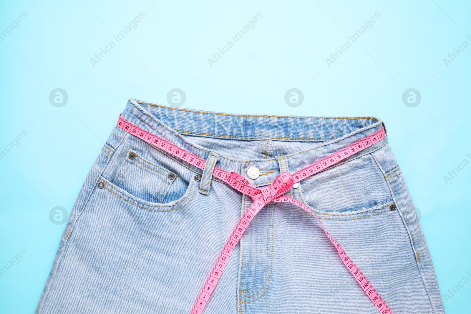 Photo of Jeans and measuring tape on light blue background, top view