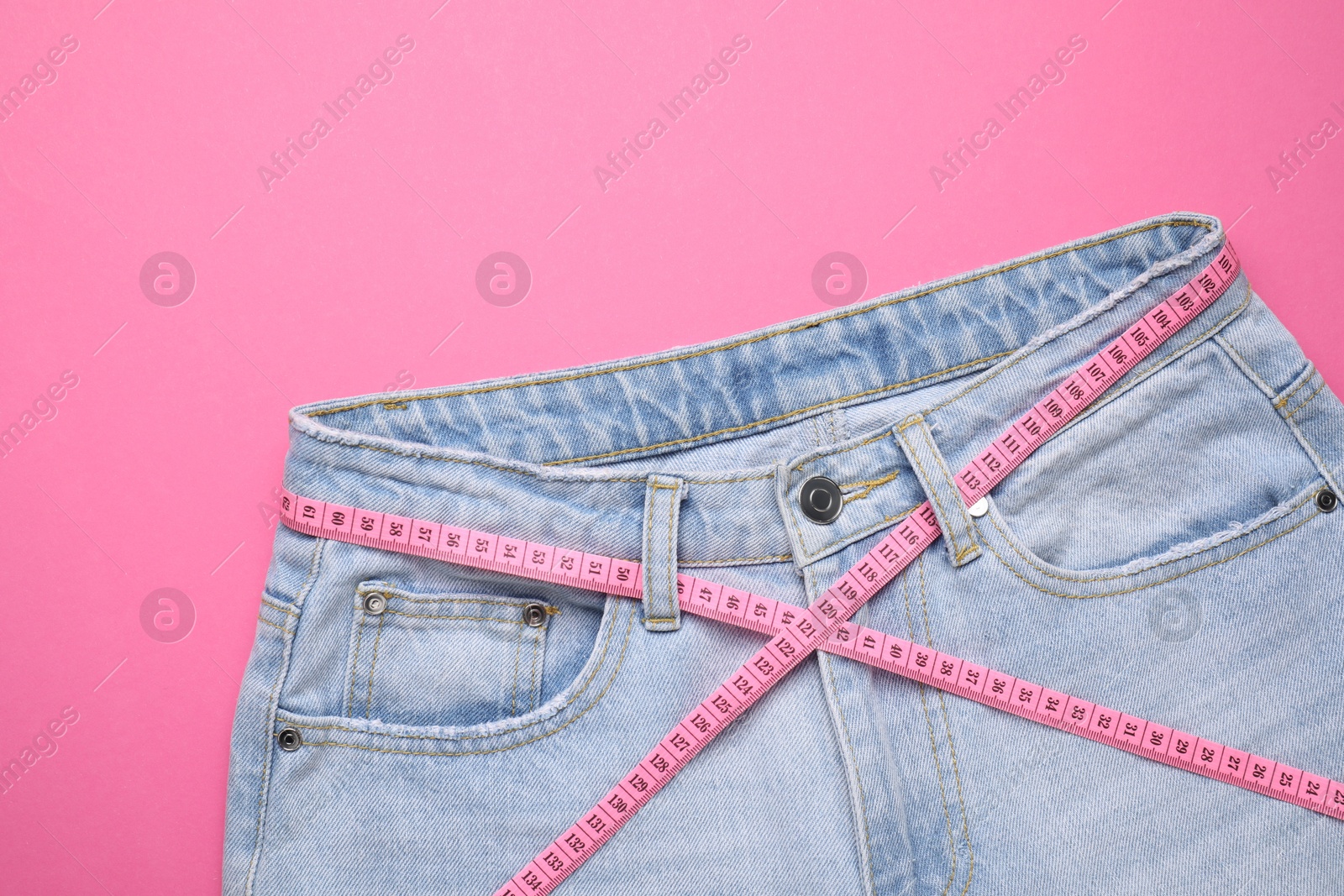 Photo of Jeans and measuring tape on pink background, top view