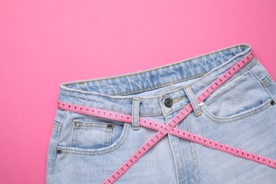 Photo of Jeans and measuring tape on pink background, top view