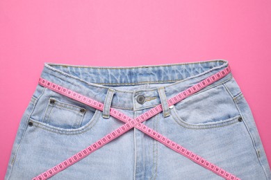 Photo of Jeans and measuring tape on pink background, top view