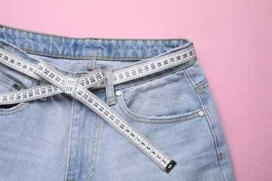 Photo of Jeans and measuring tape on pink background, top view