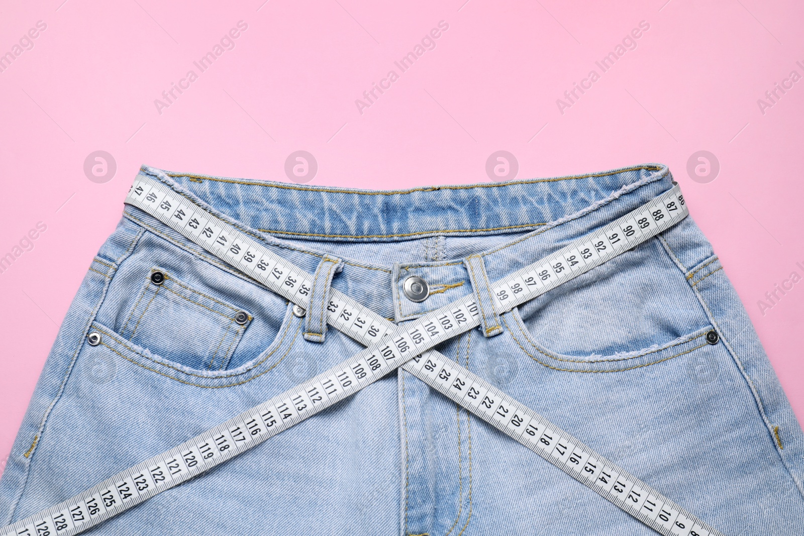 Photo of Jeans and measuring tape on pink background, top view