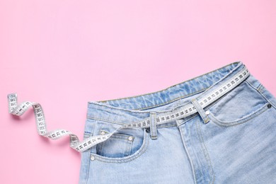 Photo of Jeans and measuring tape on pink background, top view