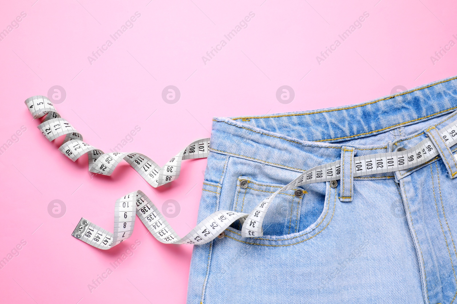 Photo of Jeans and measuring tape on pink background, top view