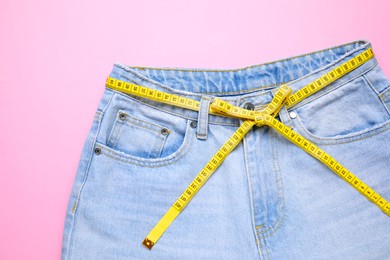 Photo of Jeans and measuring tape on pink background, top view