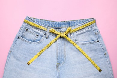 Photo of Jeans and measuring tape on pink background, top view