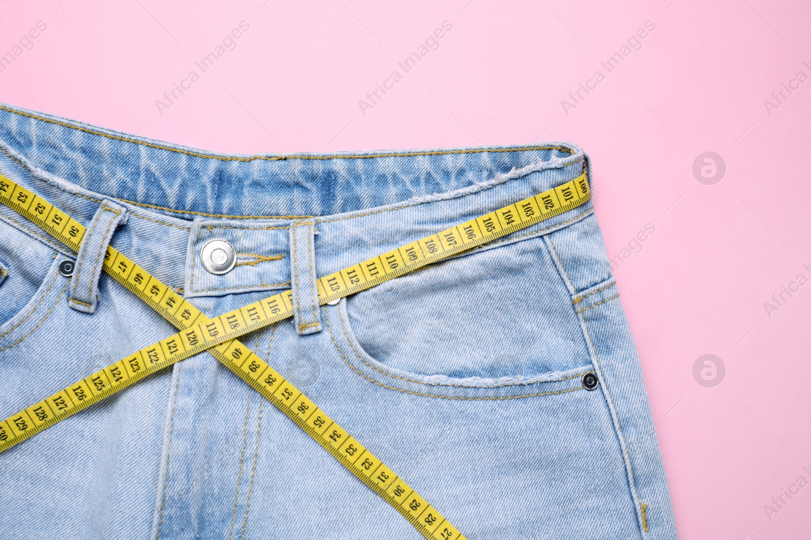 Photo of Jeans and measuring tape on pink background, top view