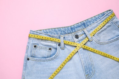 Photo of Jeans and measuring tape on pink background, top view