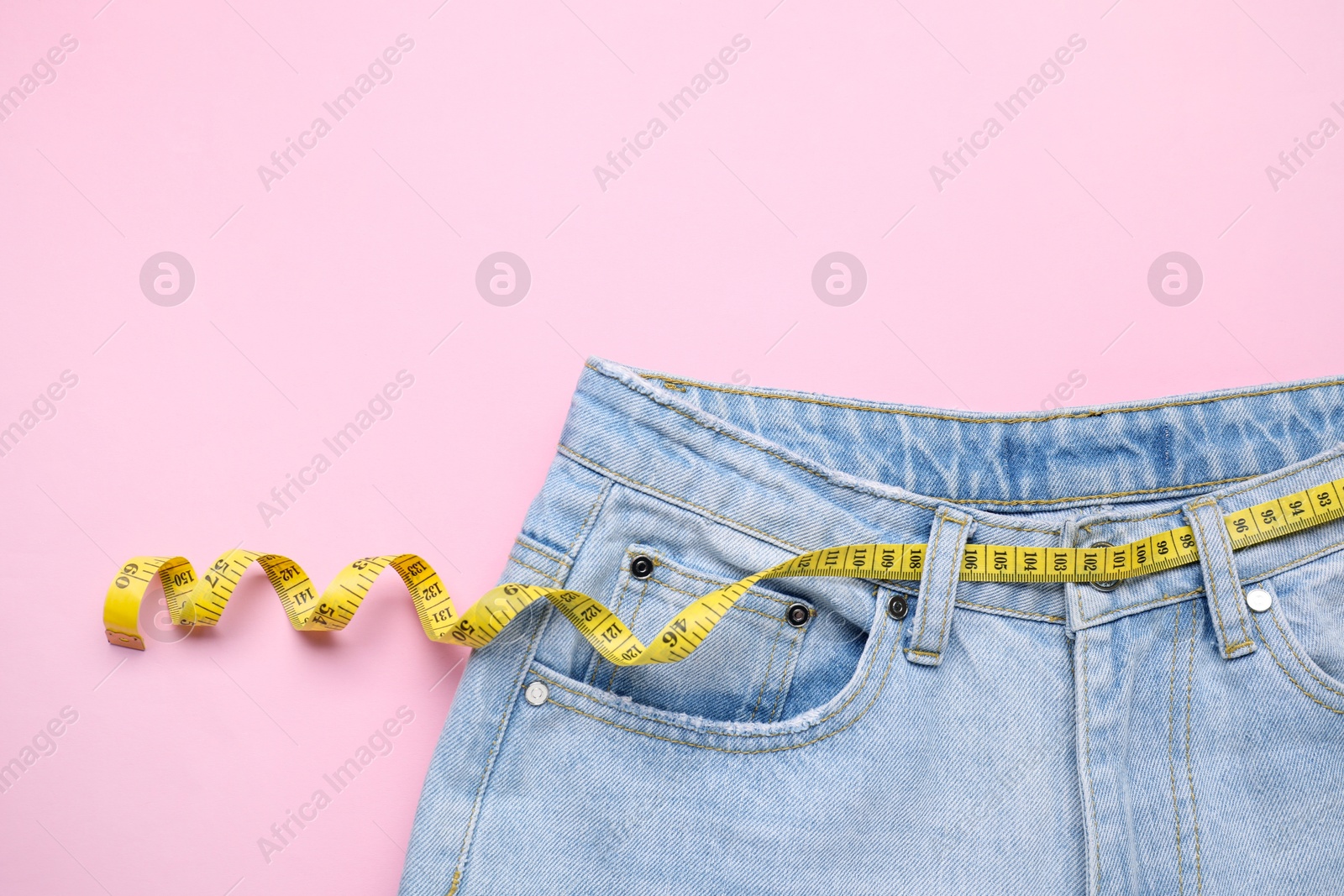 Photo of Jeans and measuring tape on pink background, top view