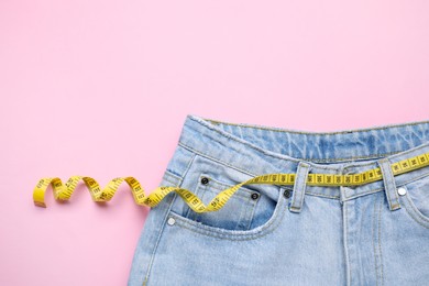 Photo of Jeans and measuring tape on pink background, top view