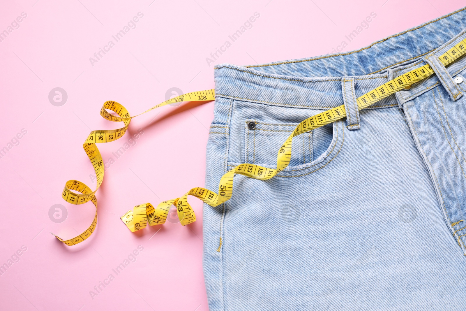 Photo of Jeans and measuring tape on pink background, top view