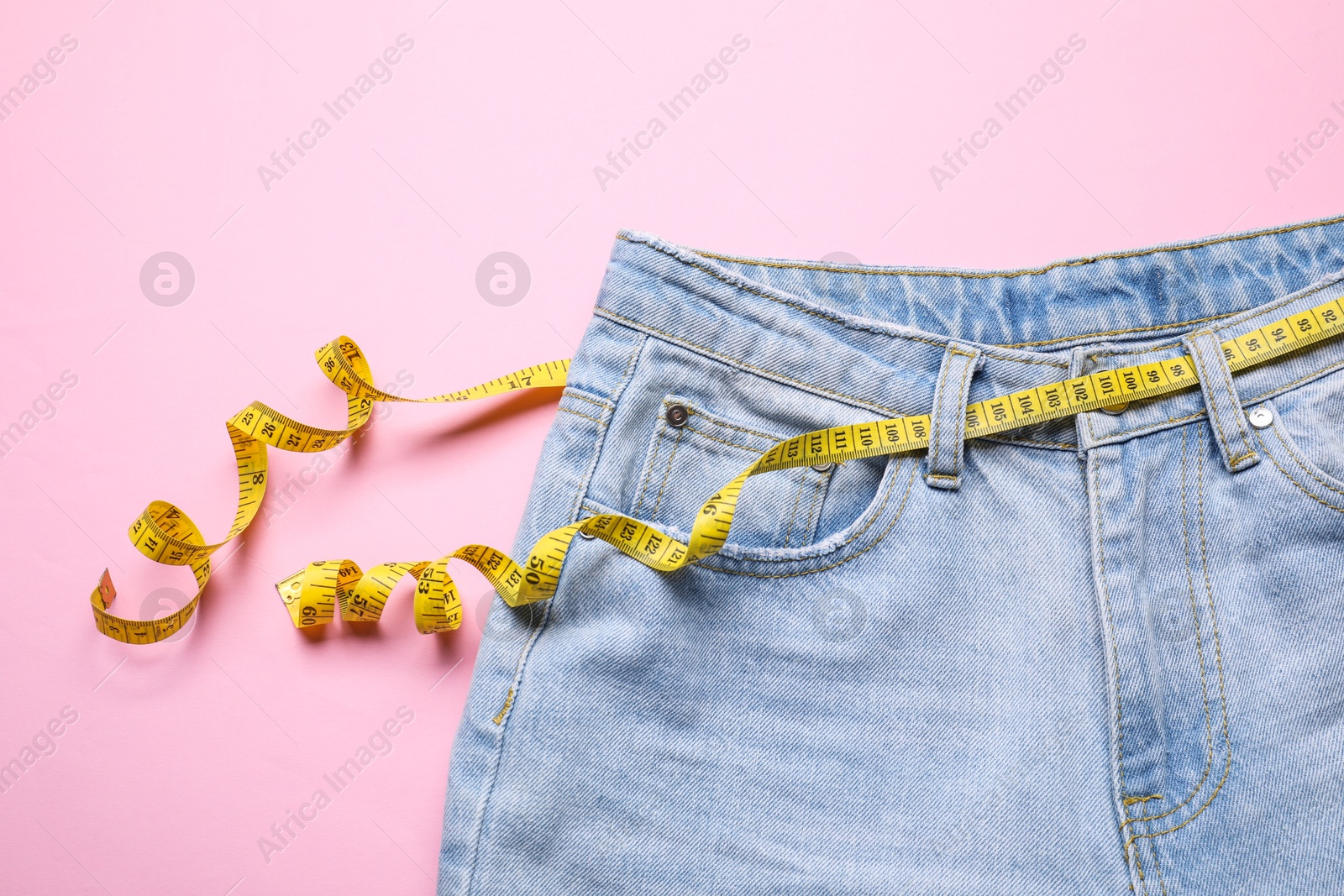 Photo of Jeans and measuring tape on pink background, top view