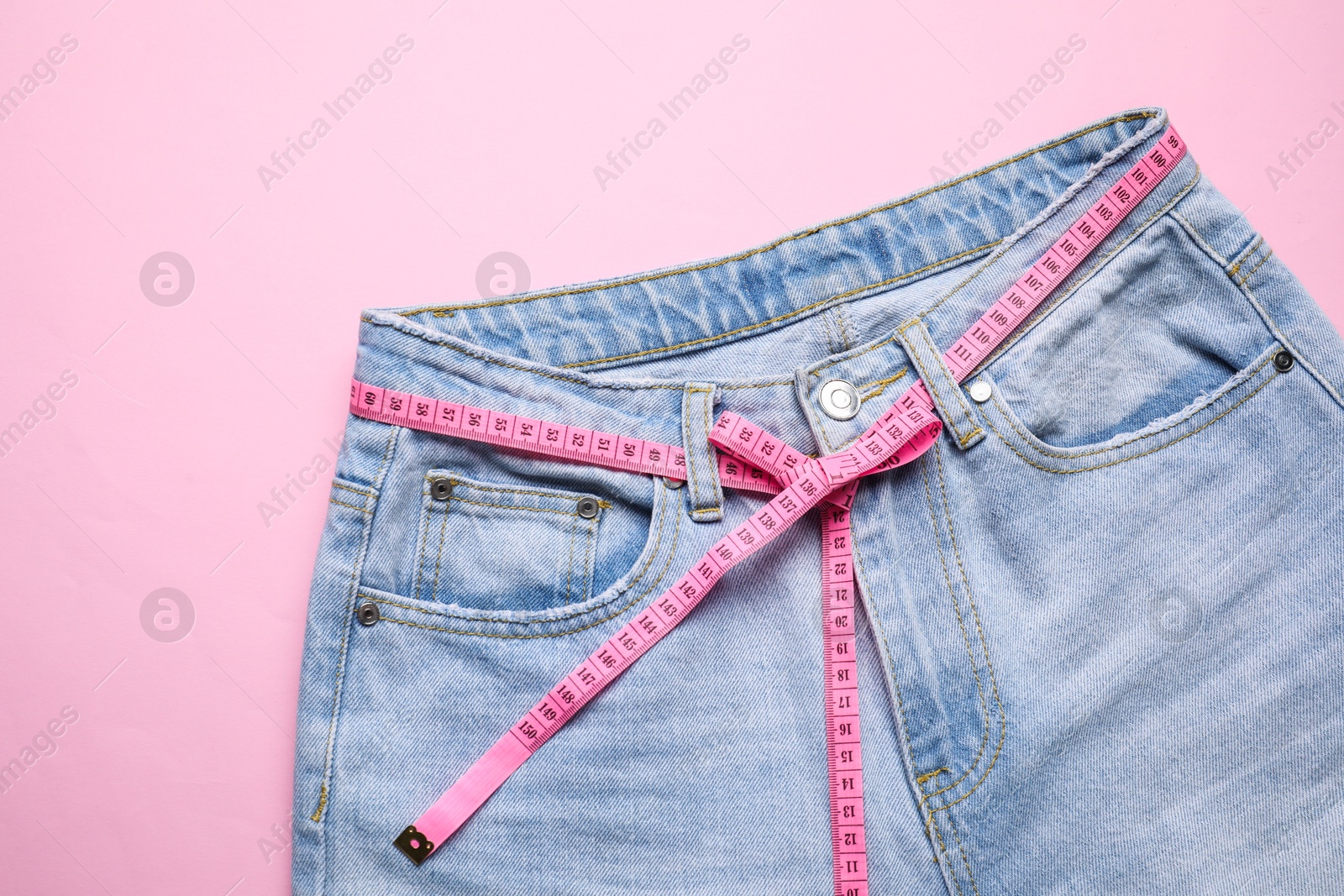 Photo of Jeans and measuring tape on pink background, top view