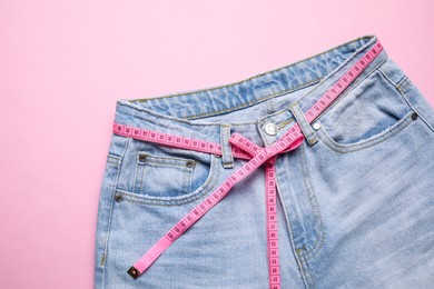 Photo of Jeans and measuring tape on pink background, top view