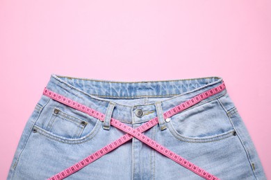 Photo of Jeans and measuring tape on pink background, top view