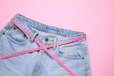 Photo of Jeans and measuring tape on pink background, top view