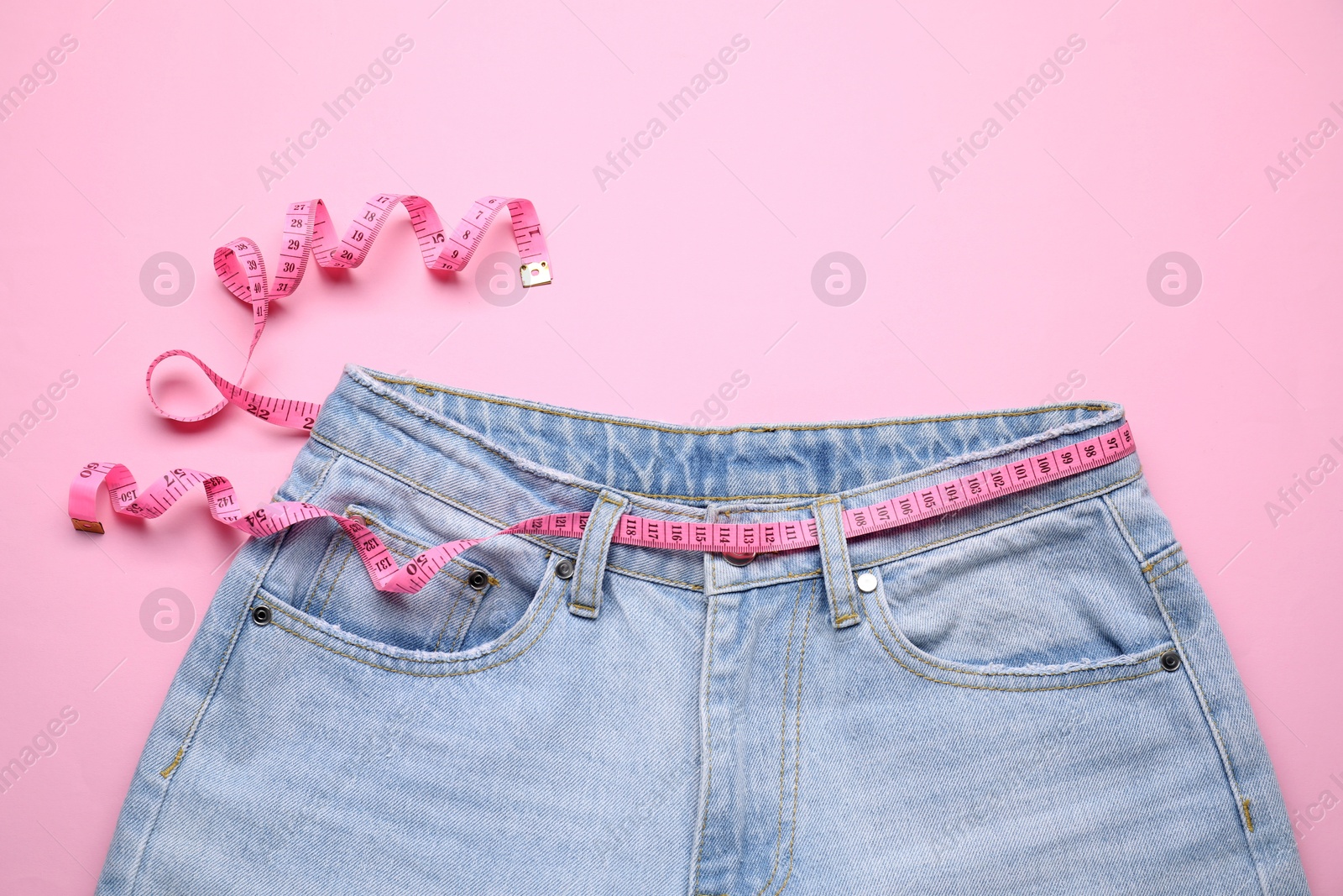 Photo of Jeans and measuring tape on pink background, top view