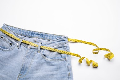 Photo of Jeans and measuring tape on white background, top view